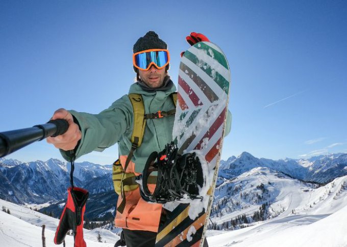 Mężczyzna na snowbordzie robi selfie przy pomocy selfie sticka z mikrofonem